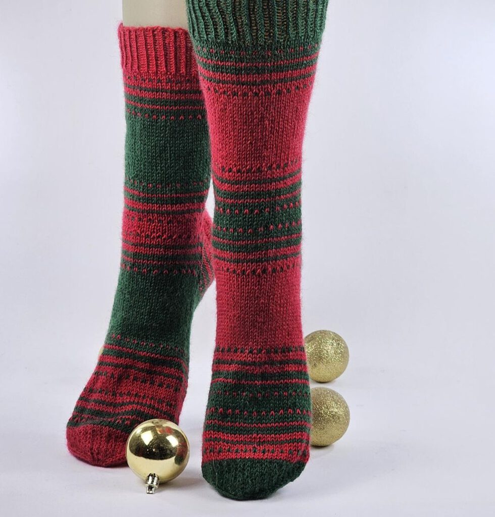 Fertig gestrickte Nebulasocks von @deuhl_strickt in Rot und Grün, am Fuß getragen auf einem hellen Hintergrund.