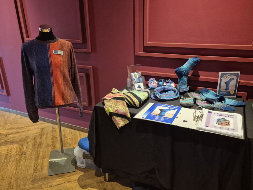 Ausstellungsstand von Plutonias Strickplanet beim Strickkino mit gestrickten Pullovern, Socken und Anleitungs-Booklets