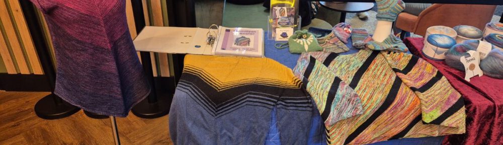 Stand von Knitting-Designerin Plutonia im Foyer des Strickkinos im Emotion Monheim mit ausgelegten Strickanleitungen und Flyern.