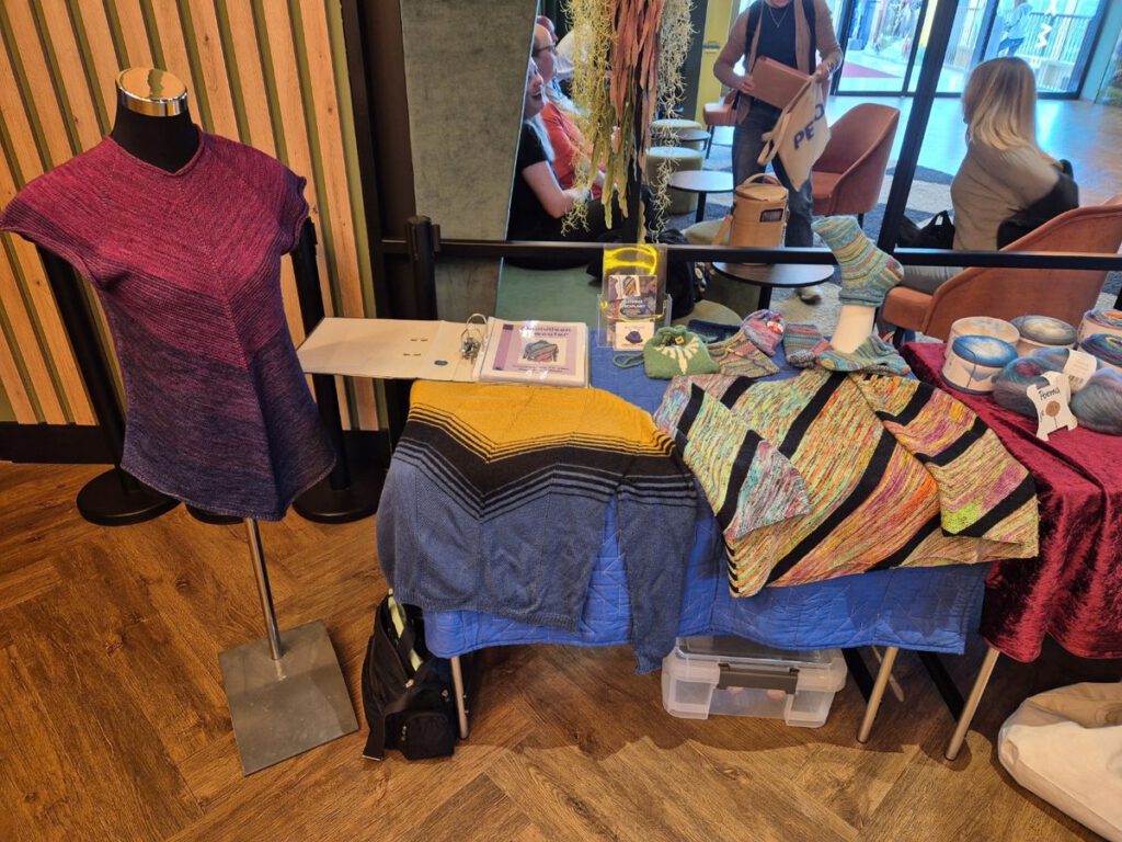 Stand von Knitting-Designerin Plutonia im Foyer des Strickkinos im Emotion Monheim mit ausgelegten Strickanleitungen und Flyern.